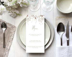 A Poppleberry neutral-shaded foliage wedding menu card, printed with 3-course dinner menu, laid on dining table with cutlery and glasses.