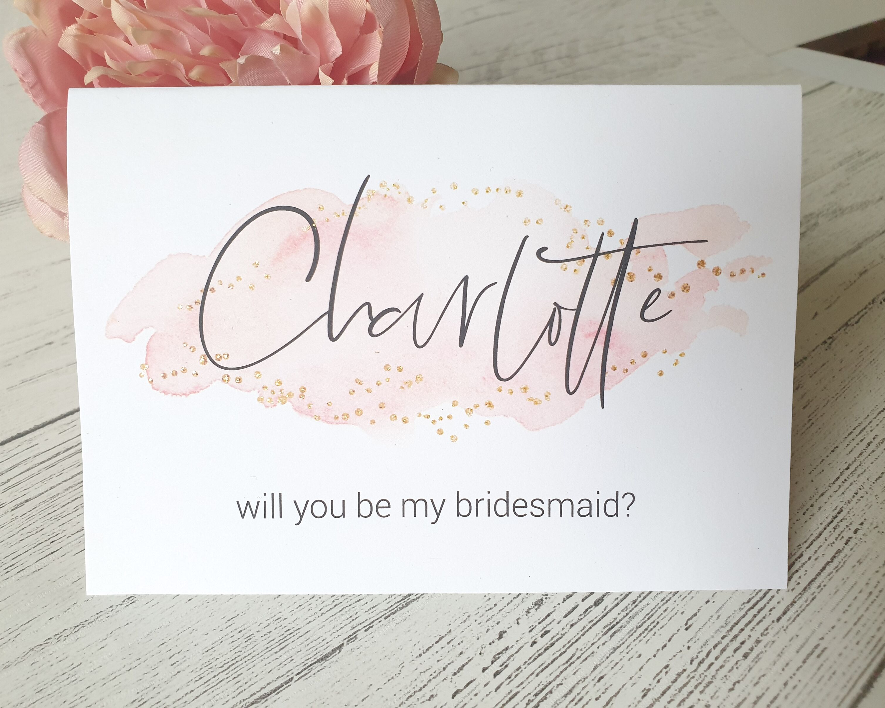 Close-up of a blush pink A6 Poppleberry 'Will you be my...?' bridesmaid proposal card with personalised name on white card