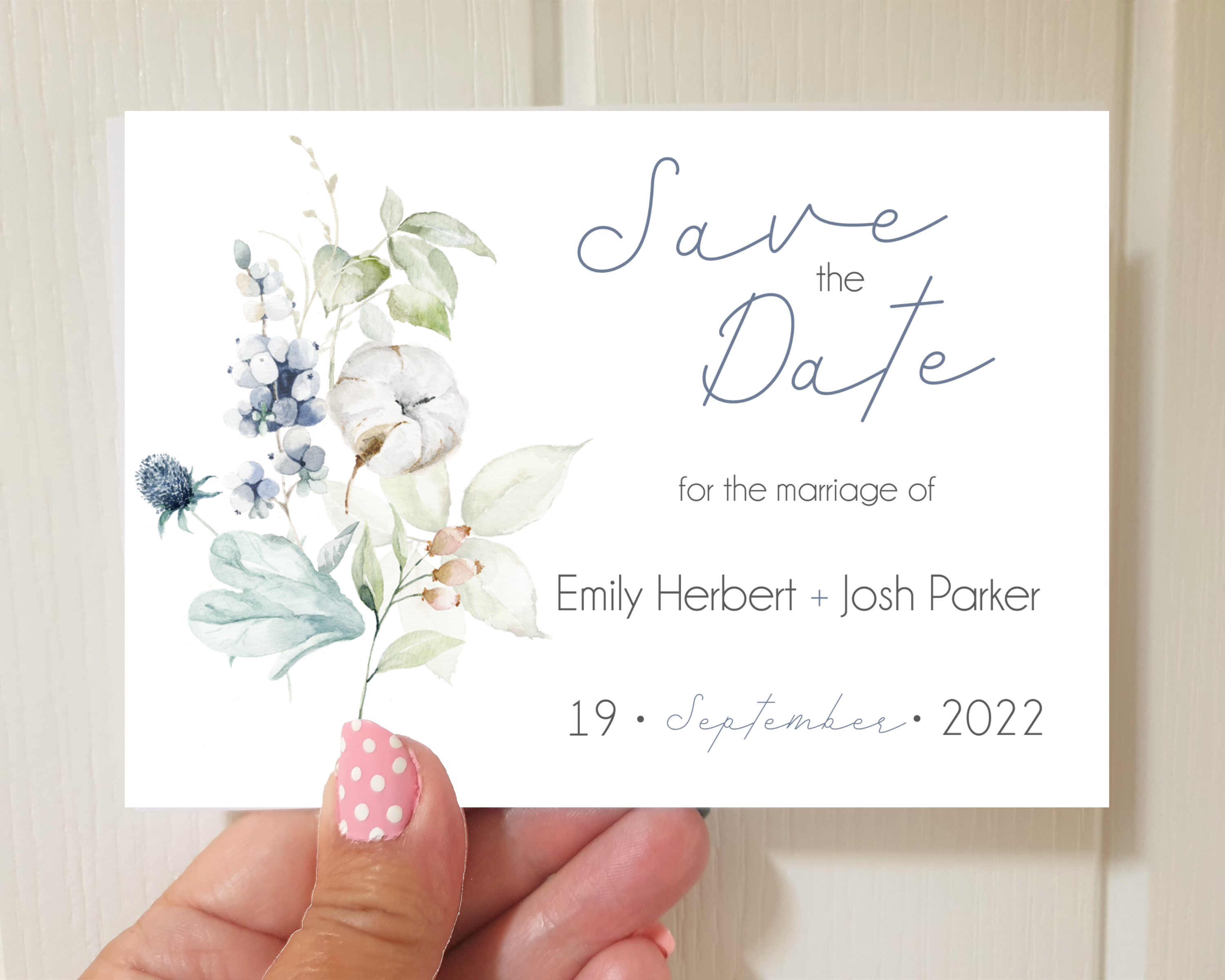 Dusty blue & cotton flowers Poppleberry A6 wedding save the date card, held to compare size to thumb.