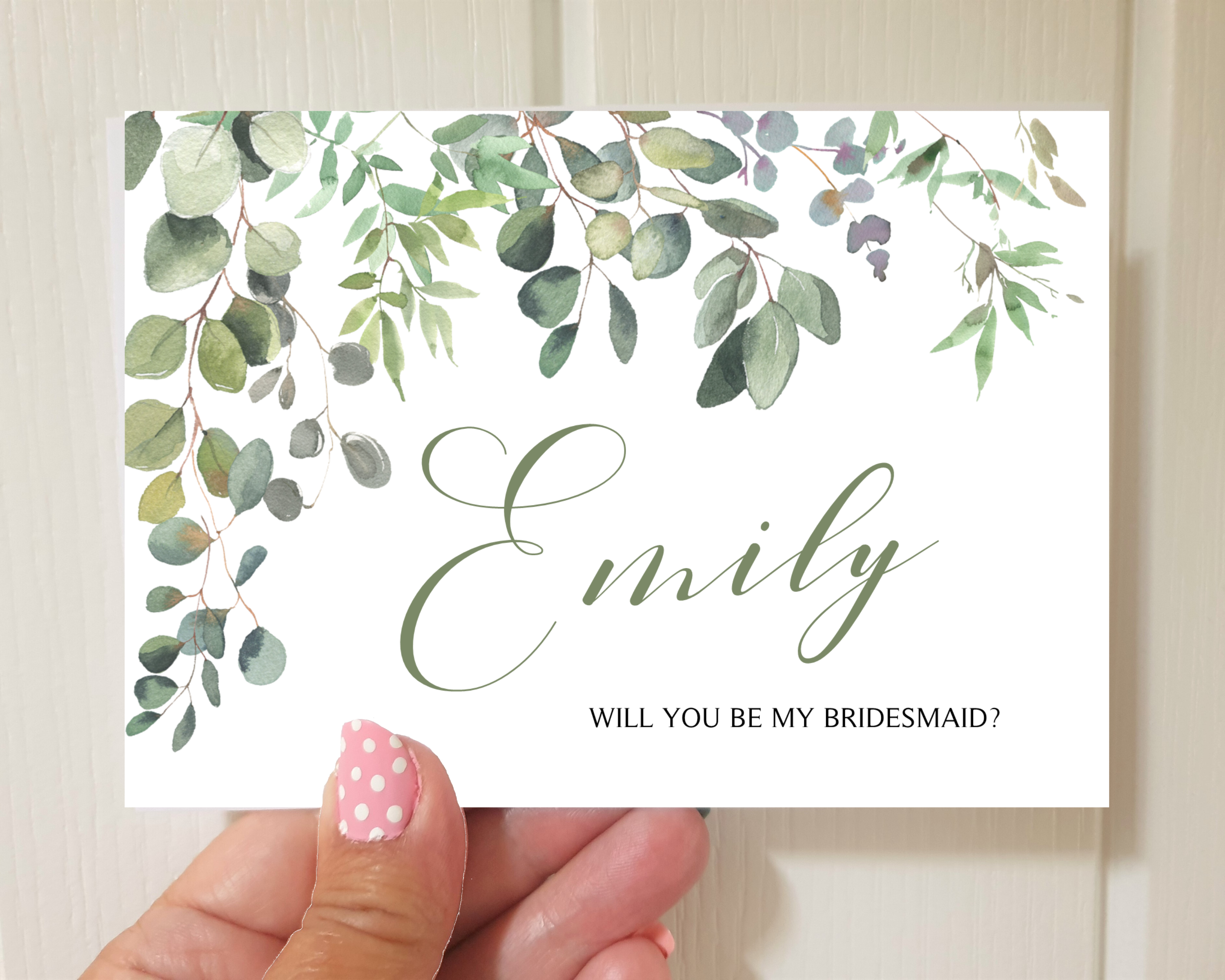 Front of a greenery & eucalyptus A6 Poppleberry 'Will you be my...?' bridesmaid proposal card, held to show size.