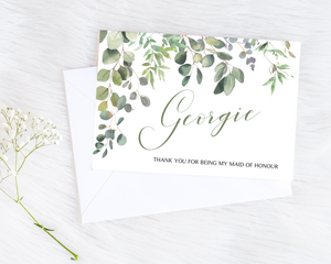 Front of a greenery & eucalyptus A6 Poppleberry bridesmaid thank you card with personalised name and white envelope.