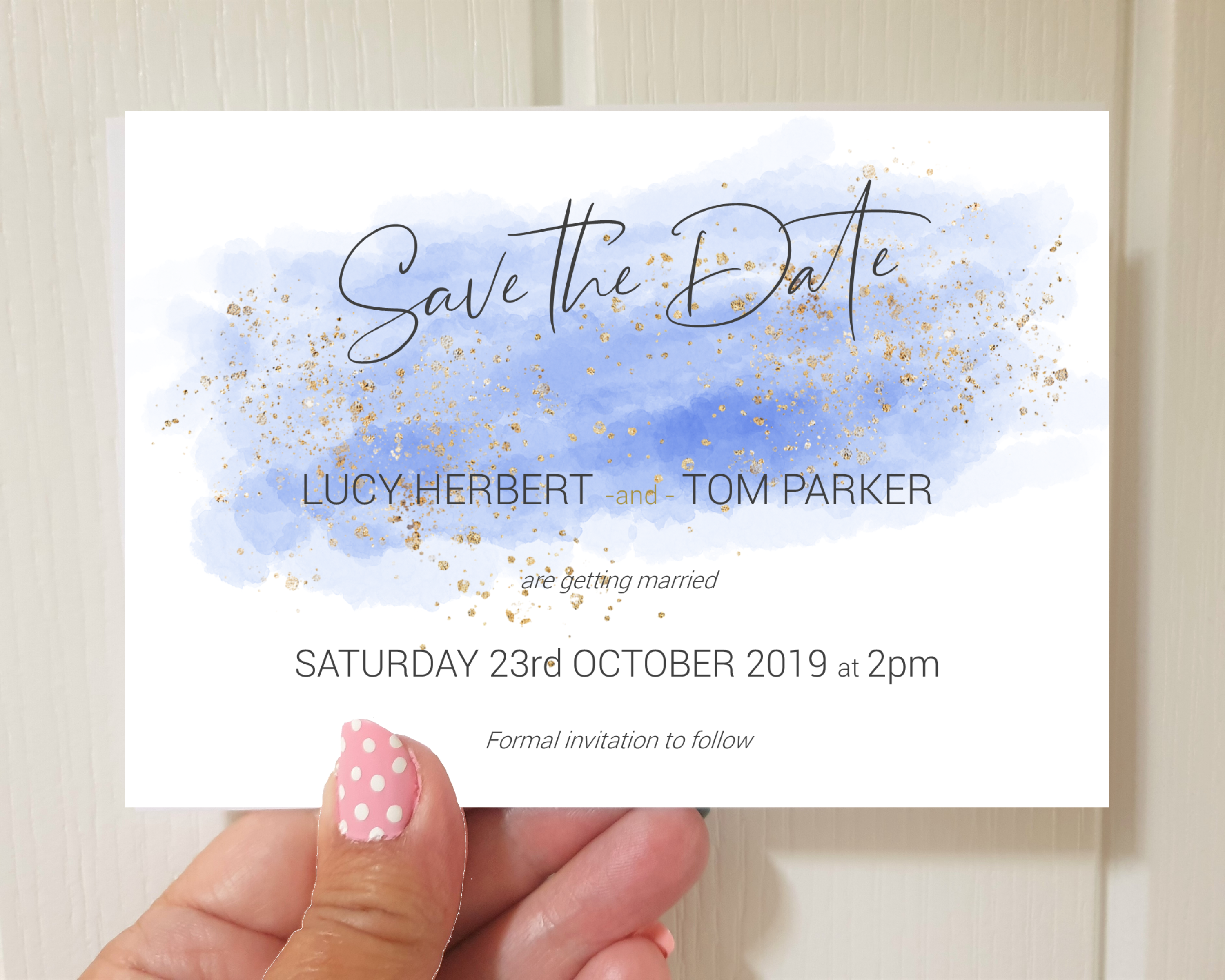 A watercolour blue A6 Poppleberry one-sided wedding save the date card, with gold sparkles, held up.