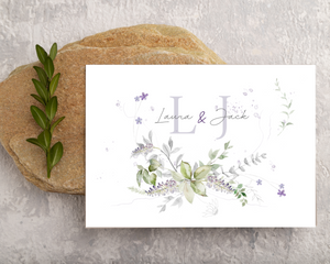 Close-up of a lavender & greenery A6 Poppleberry accordion fold all-in-one wedding invitation, folded on a stone.