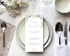 A Poppleberry dusty blue & cotton flowers wedding menu card, printed with 3-course dinner menu, laid on dining table with cutlery and glasses.