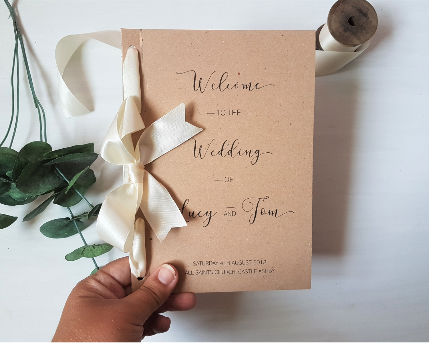 Size of the rustic kraft brown A5 Poppleberry folded wedding order of service card compared to the size of a hand.