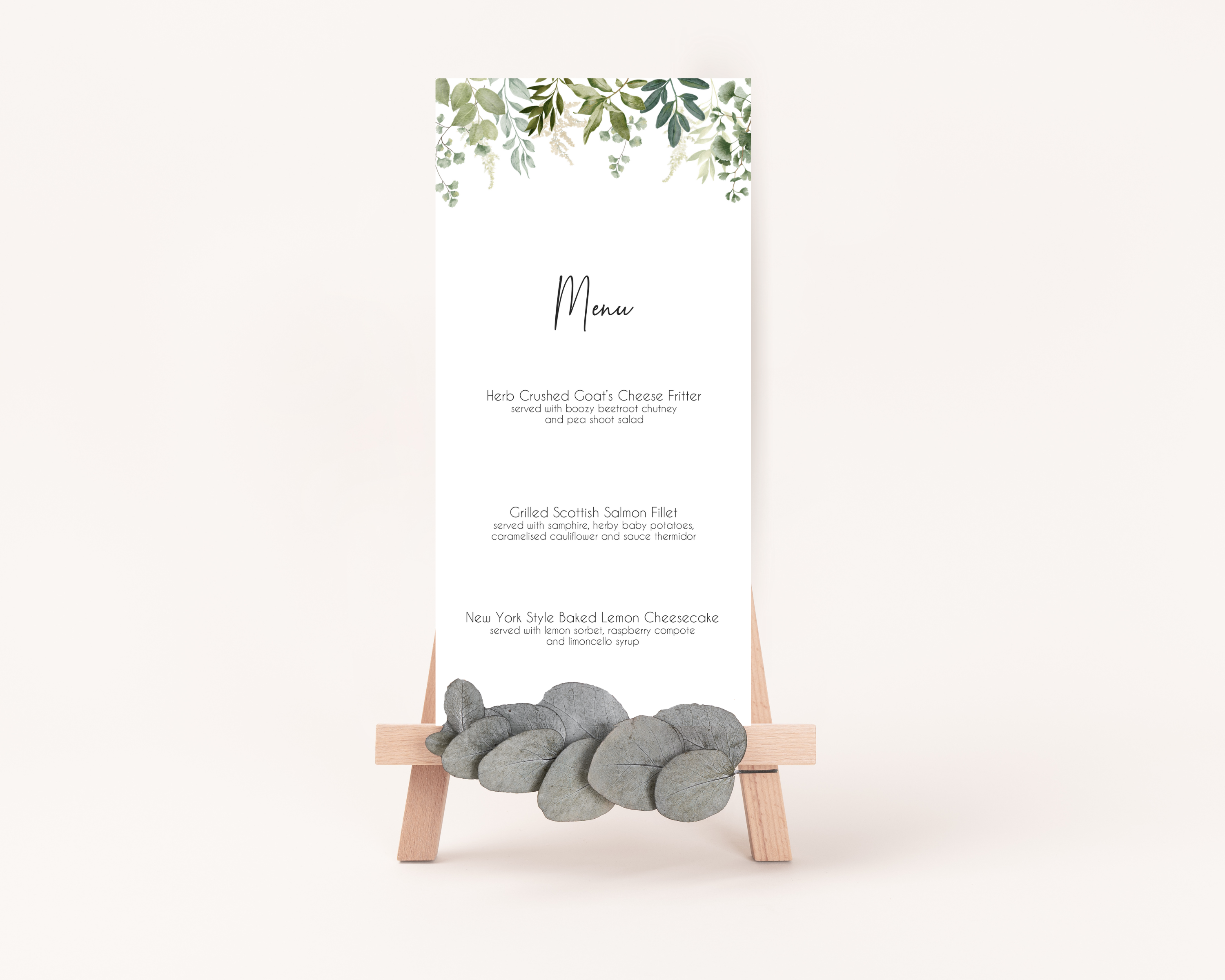 A Poppleberry greenery & eucalyptus wedding menu card, printed with 3-course dinner menu, stood up on easel with matching leaves.