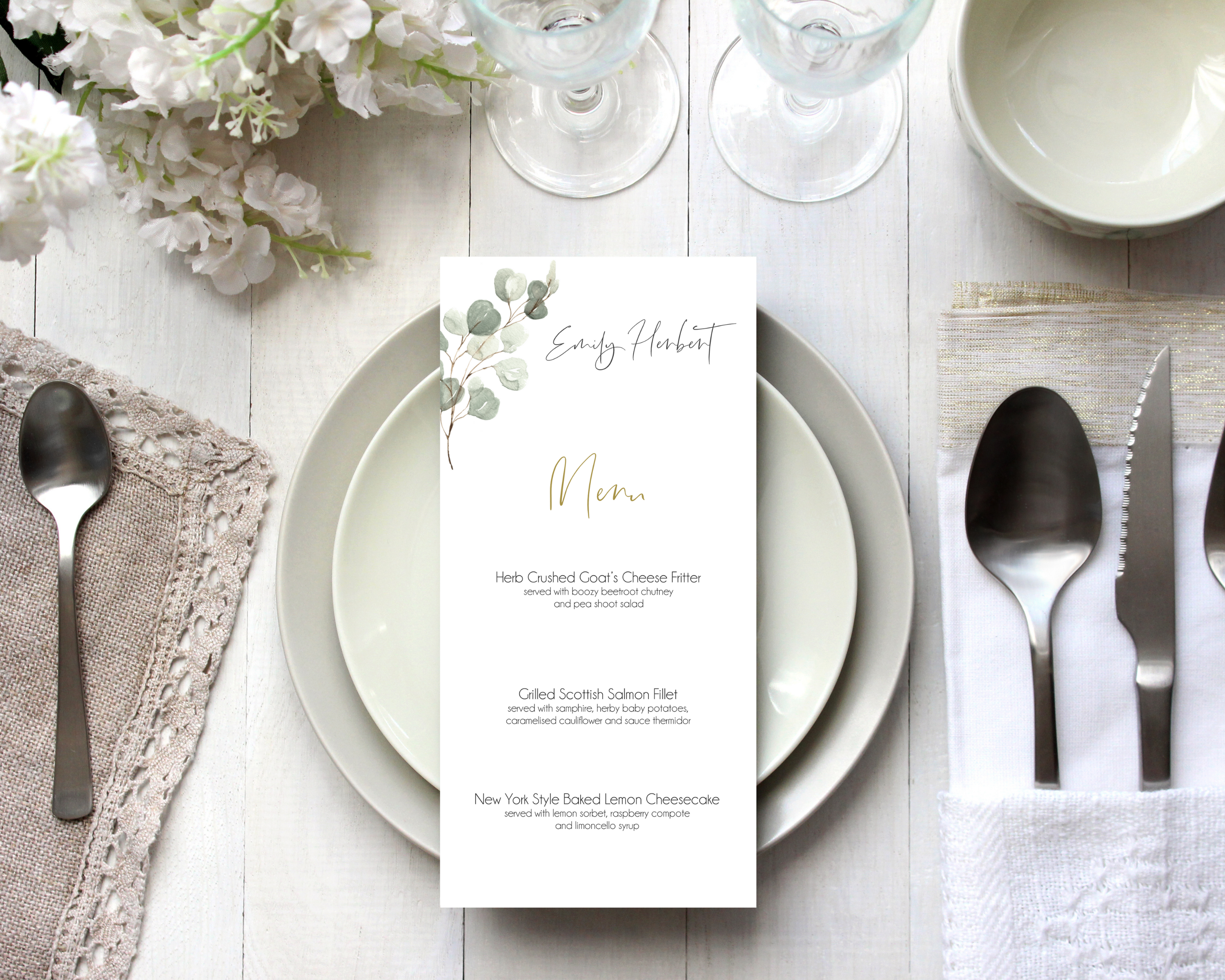 A Poppleberry muted green eucalyptus wedding menu card, printed with 3-course dinner menu, laid on dining table with cutlery and glasses.
